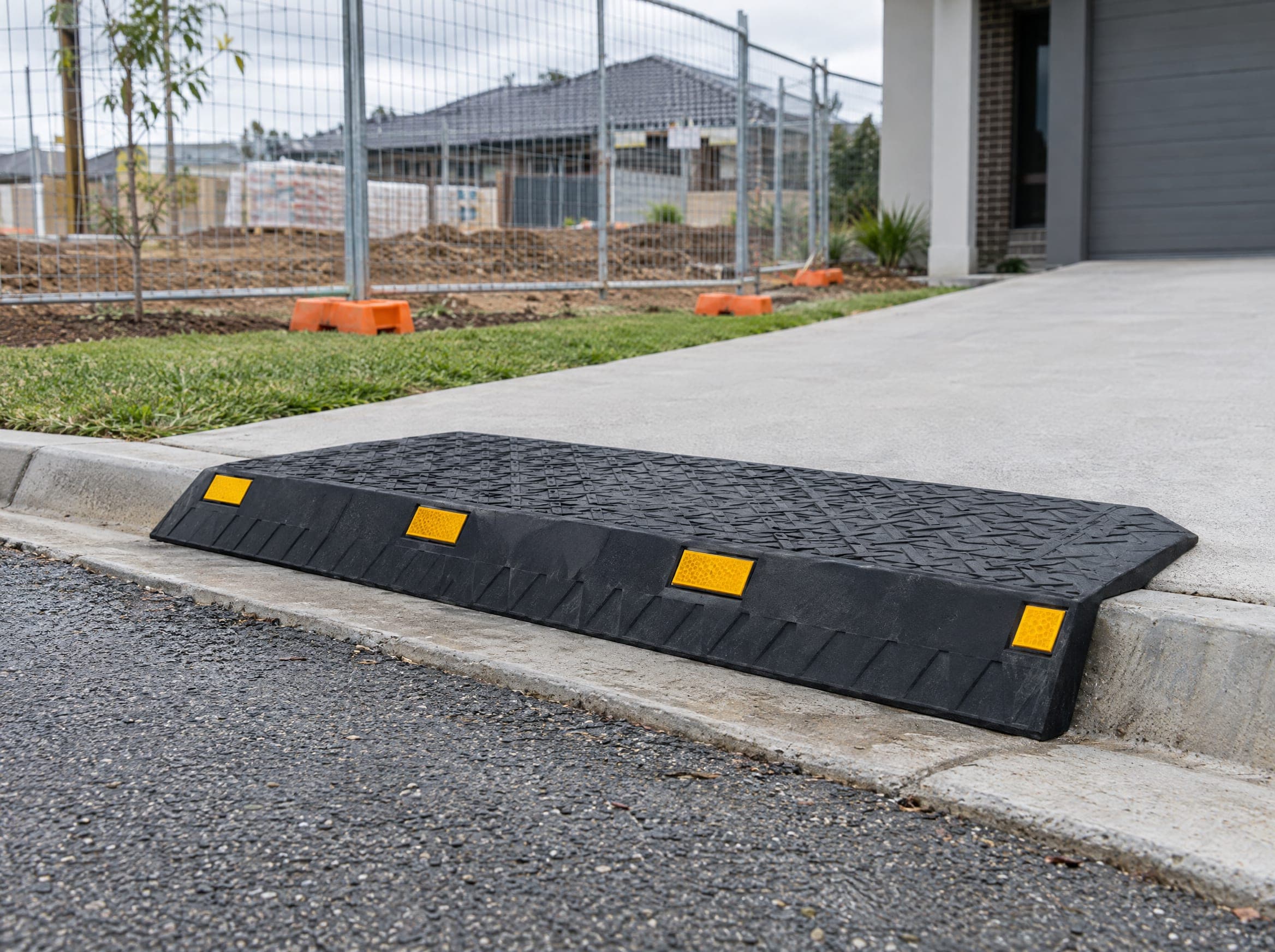 A black rubber kerb ramp with yellow reflectors at a building site driveway